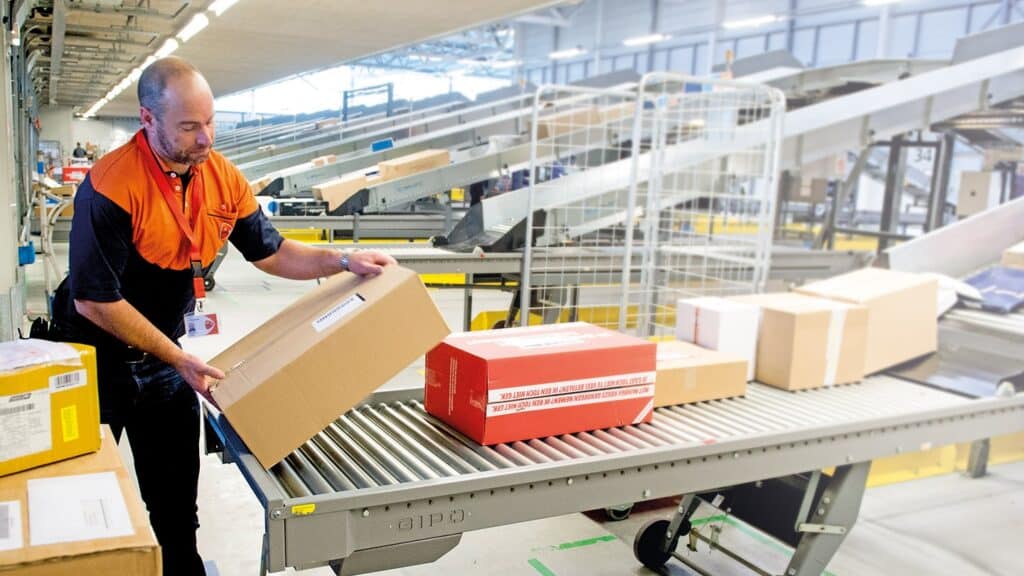 PostNL employee handling parcels on a conveyor belt Man in PostNL magazijn sorteert pakketten op de lopende band.